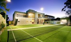 a tennis court in front of a house with lights on the side of it at night