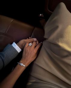 two people holding hands on the back of a brown leather couch in front of a pillow