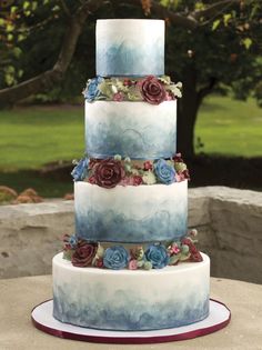 a three tiered cake with blue and red flowers on it's side sitting on a table