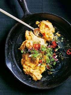 scrambled eggs in a skillet with garnish and a spoon on the side