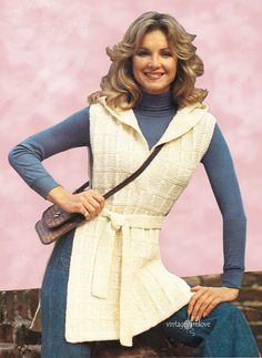 a woman wearing a white vest and blue shirt is posing for the camera with her hands on her hips