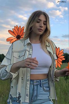 a woman standing in a field with an orange flower on her shirt and jeans shorts