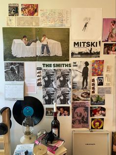 a wall covered with posters and pictures next to a laptop computer on top of a wooden desk