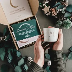 a person holding a coffee cup in front of a box with the word joy on it