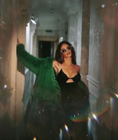 a woman in black dress and green jacket posing for the camera with bubbles around her