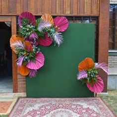 some pink and orange flowers are hanging on a green wall next to a red rug