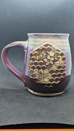 a purple and gold coffee mug sitting on top of a gray cloth covered tablecloth