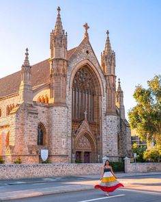 a woman is walking across the street in front of an old church with tall towers