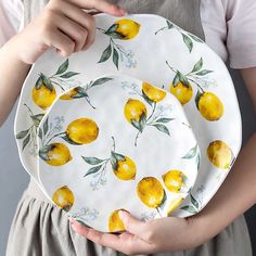 a woman holding two plates with lemons painted on them, one is white and the other is yellow