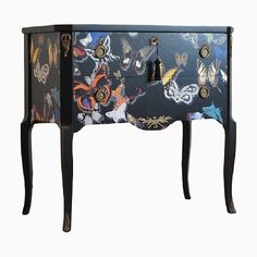 an ornate black and multicolored cabinet with butterflies painted on the doors, drawers and handles