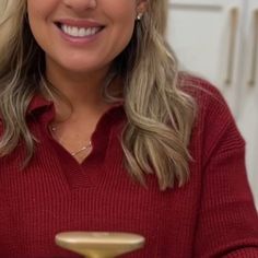 a woman in a red sweater is holding a gold object and smiling at the camera