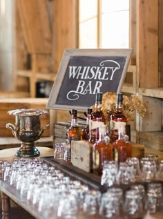 a wooden table topped with lots of glasses next to a sign that says whiskey bar