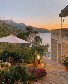 an outdoor patio with tables and umbrellas next to the water at sunset or dawn