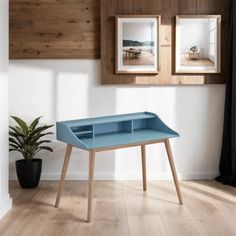 a blue desk with two pictures on the wall above it and a potted plant next to it