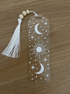 an acrylic bookmark with tassels and stars on it, sitting on a wooden surface