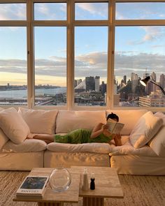 a woman laying on top of a white couch in front of a window reading a book