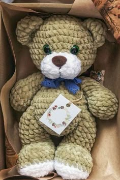 a brown teddy bear sitting in a box with a tag on it's chest