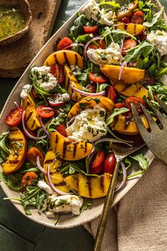 a salad with grilled peaches, tomatoes and feta cheese on it next to a fork