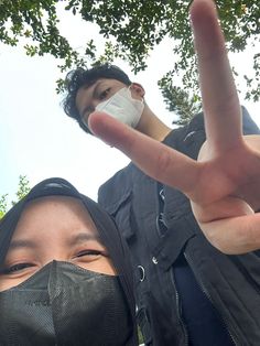 two people wearing face masks making the peace sign with their fingers in front of them