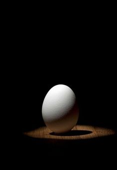 an egg sitting on top of a wooden table next to a black wall and floor