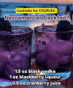 two glasses filled with purple liquid and topped with blackberries, sitting on the beach