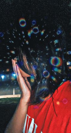 a woman blowing bubbles in the air with her hands on her face and looking into the distance