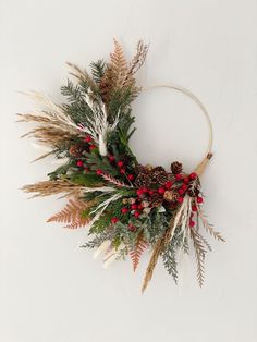 a wreath with red berries, pine cones and greenery is hanging on the wall