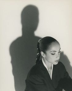 a black and white photo of a woman sitting in front of a man's shadow