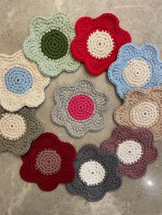 six crocheted flower coasters arranged in a circle on a gray surface with white and red circles