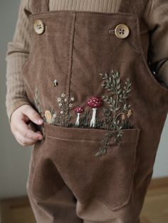 a person holding a pocket with mushrooms and plants in it, while wearing brown overalls