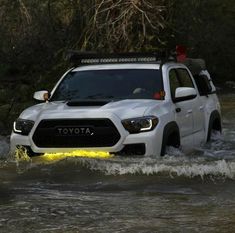 a white truck driving through a river with yellow lights on it's front bumper