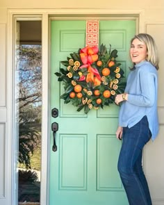 a woman standing in front of a green door with a wreath on it and oranges