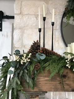 a mantel with candles, greenery and pine cones