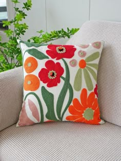 an orange and green flowered pillow sitting on top of a white couch next to a potted plant