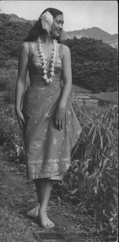 an old black and white photo of a woman standing in front of some bushes with flowers on her head