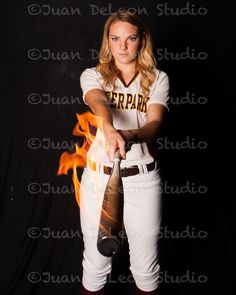 a female baseball player holding a bat in front of a black background with fire behind her