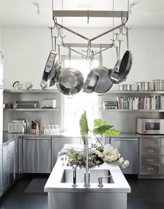 a kitchen with pots and pans hanging from the ceiling above the sink, surrounded by stainless steel appliances