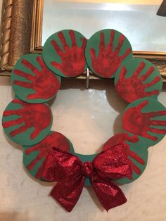 a handprinted christmas wreath with red and green paper on it, sitting in front of a mirror