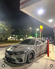 a silver car is parked at a gas station with its hood up and lights on