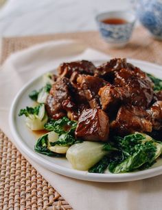 a white plate topped with meat and veggies on top of a woven table cloth