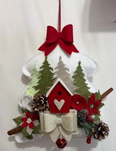 a christmas ornament hanging on the wall with pine cones, holly and a red birdhouse