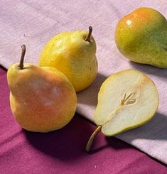 three pears and one apple on a purple cloth