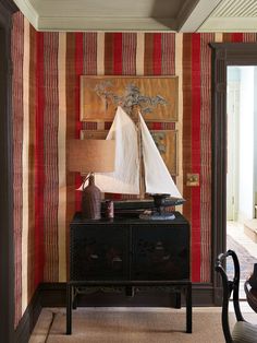 a small sailboat is sitting on top of a dresser in a room with striped walls