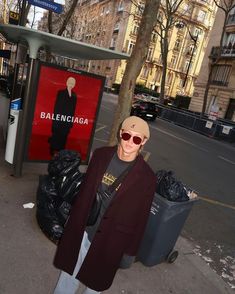 a woman standing on the sidewalk in front of a bus stop with bags and trash