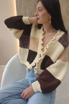 a woman sitting on top of a white chair wearing a brown and tan striped sweater