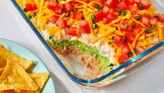 a casserole dish with tortilla chips and tomatoes on the side next to it