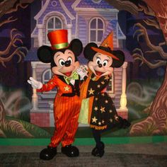 two mickey and minnie mouse characters in front of a house with halloween decorations on it