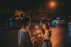 a man and woman holding sparklers in their hands on the street at night time