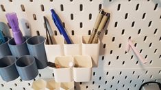 several pens, markers and pencils are arranged on a white pegboard with holes in it