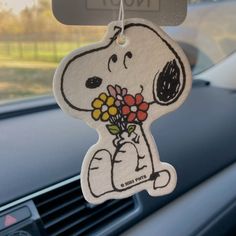 a snoopy car air freshener hanging from the dash board with flowers in it